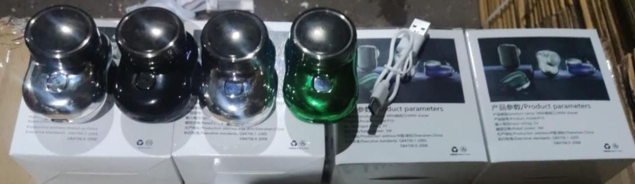 Set of four metallic objects with a green one on a white surface, with a box and additional items in the background.